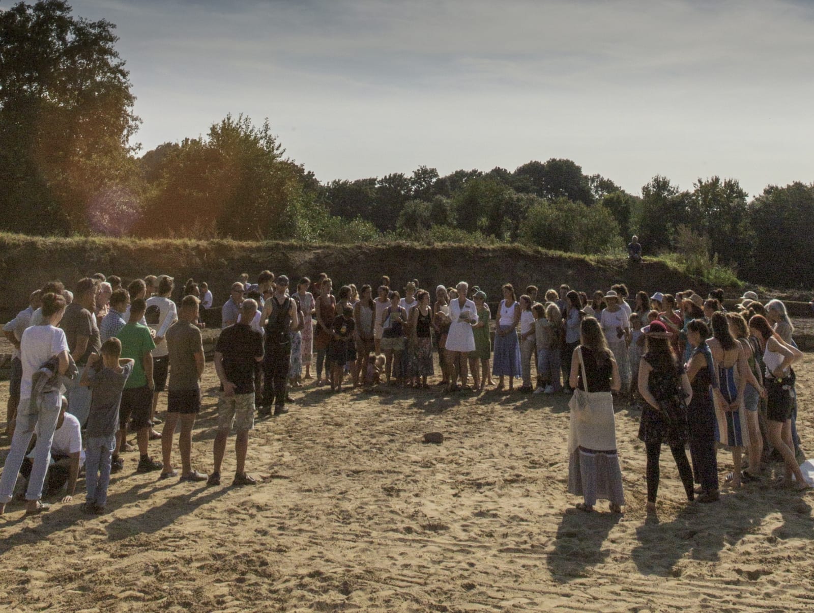 Eine große Gruppe Menschen steht im Kreis auf einem Feld in der Abendsonne